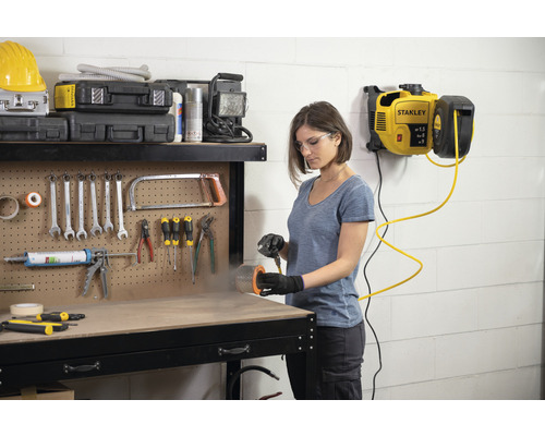 Vrouw werkt met een Stanley luchtcompressor in een werkplaats. Verschillende gereedschappen zijn bevestigd aan een werkbank.