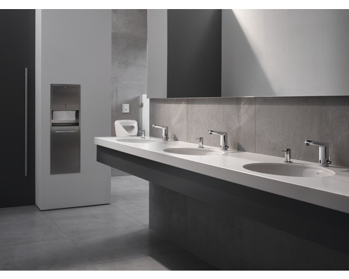 Openbare wasruimte met wastafels, kranen, zeepdispensers en een papierhanddoekdispenser.