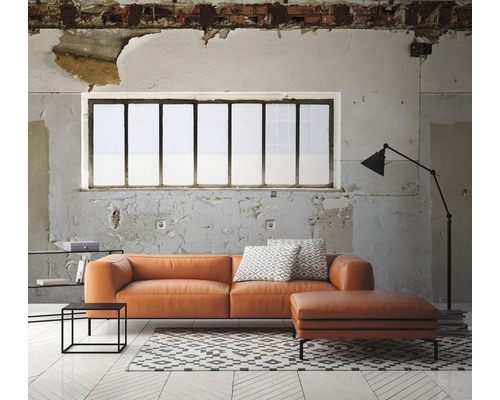 Woonkamer met oranje leren bank, ottomane, vloerkleed en staande lamp voor een raam