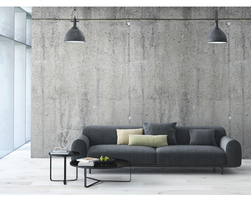 Woonkamer met grijze bank, salontafel en hanglampen voor een betonnen muur.