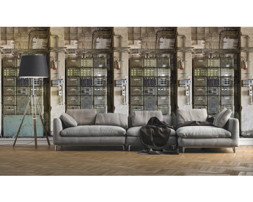 Woonkamer met grijze bank, staande lamp en wandbehang met schakelkastmotief voor een industriële sfeer.