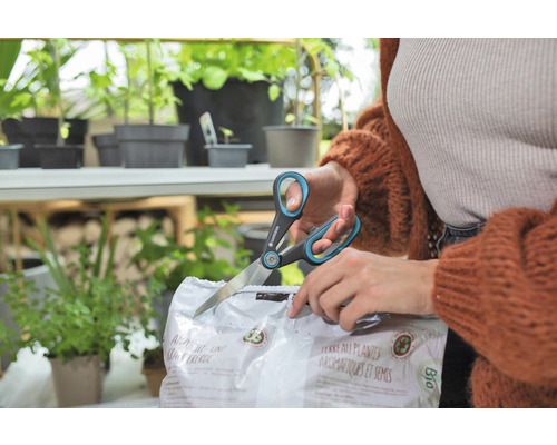 Een persoon opent een verpakking zaai- en kruidenaarde met een schaar van het merk Gardena.