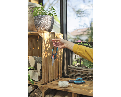 Tuinscene met plantenbak, houtblokken, tuinschaar en een persoon