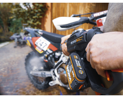 Een persoon maakt een motorfiets schoon met een draadloze hogedrukreiniger.