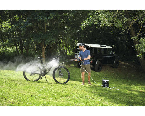 Een man reinigt een fiets met een mobiele hogedrukreiniger in de buitenlucht.