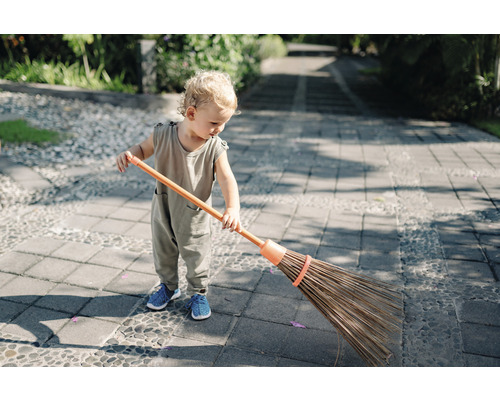 Een kind veegt een betegeld pad met een bezem.