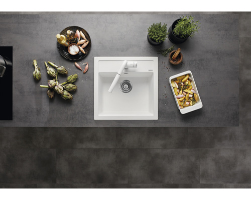 Keuken spoelbak met kraan, omringd door artisjokken, kruiden en bereide gerechten op een aanrecht.