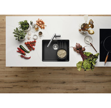 Keukenscène met spoelbak, kraan, kruiden, groenten en kookgerei op een aanrecht.