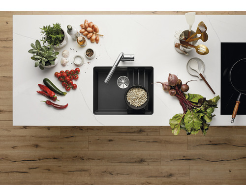 Keukenscène met spoelbak, kraan, kruiden, groenten en kookgerei op een aanrecht.