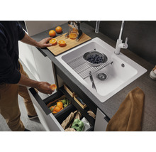 Keukenscène met spoelbak, kraan, snijplank, citruspers en afvalemmer onder de spoelbak.