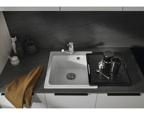 Keuken spoelbak met afdruiprek, kraan en keukengerei op een aanrecht.