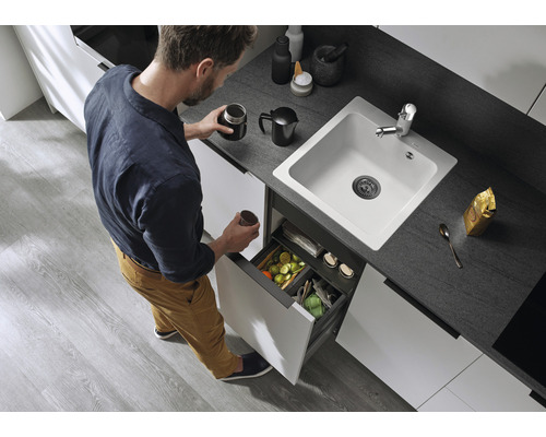 Een man in een keuken met een witte spoelbak en een afvalscheidingssysteem