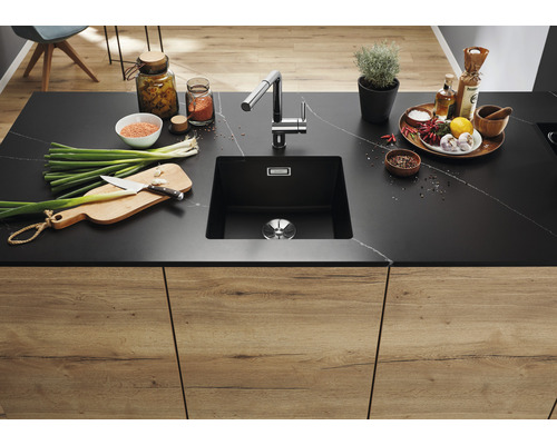 Keukenspoelbak van zwart materiaal met kraan in een moderne keuken met etenswaren op het aanrecht