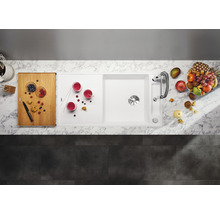 Bovenaanzicht van een spoelbak met afdruiprek, kraan, snijplank, drankjes en fruit.