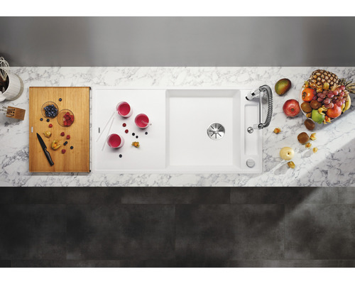 Bovenaanzicht van een spoelbak met afdruiprek, kraan, snijplank, drankjes en fruit.