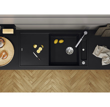 Zwarte gootsteen met afdruiprek, kraan, citroenen en mes op een aanrecht.