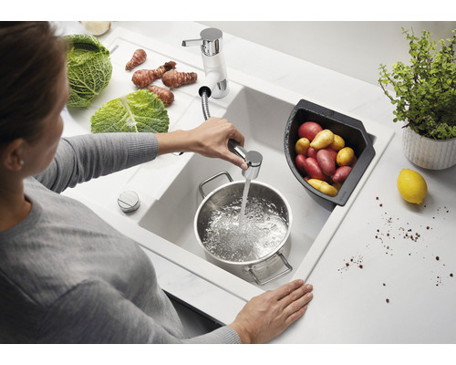 Vrouw vult pan met water in een gootsteen met groenten