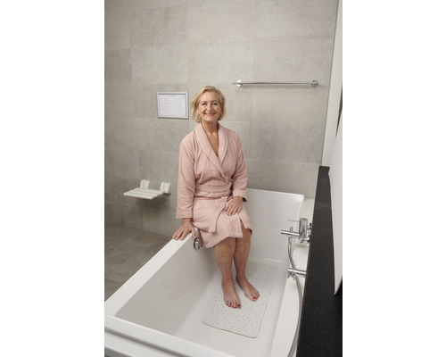 Een vrouw zit in een seniorenvriendelijke badkamer op de rand van een bad met antislipmat.