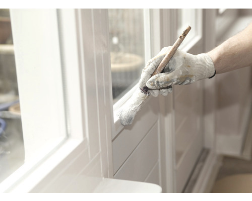 Een persoon schildert een wit raamkozijn met een kwast.