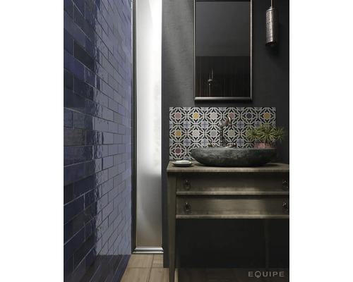 Badkamer met stenen wastafel op houten commode, blauwe tegels op de muur en tegels met patroon boven het dressoir