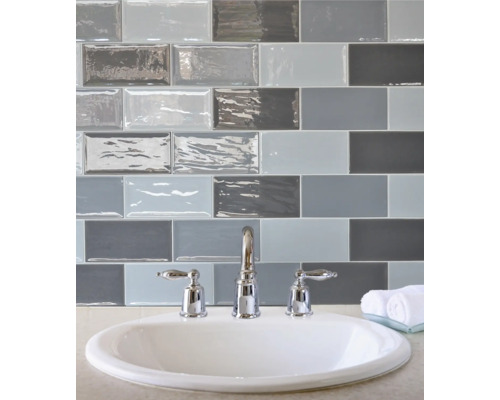 Wastafel met kraan voor een muur van rechthoekige tegels in verschillende grijstinten