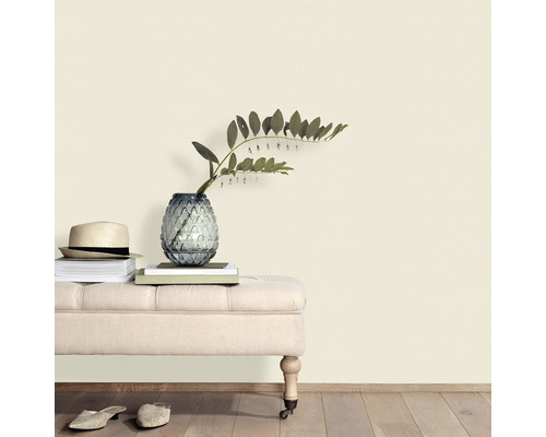 Decoratieve scène met zitbank, vaas, planten, boeken en hoed tegen een muur.