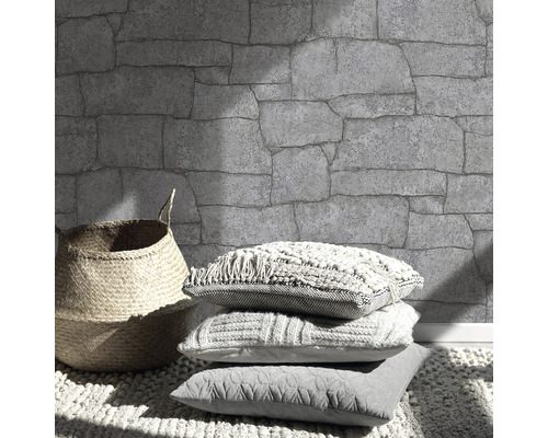 Muur met steenmotief, mand en kussens op een vloerkleed.