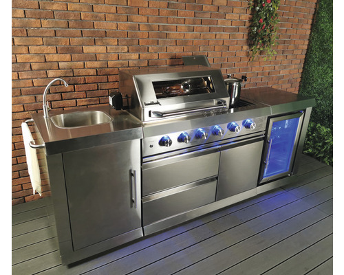 Roestvrijstalen buitenkeuken met spoelbak, barbecue, koelkast en opbergruimte tegen een bakstenen muur.