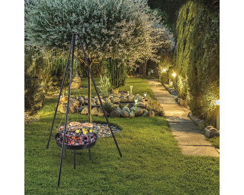 Barbecue met driepoot in de tuin met bomen, stenen en gazon