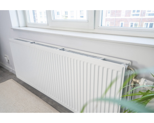 Witte paneelradiator onder een raam in een heldere kamer