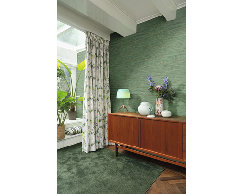 Woonkamer met groen textielbehang, tapijt, gordijnen en houten dressoir