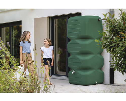 Scene met twee meisjes en een groene regenwatertank voor een huis.