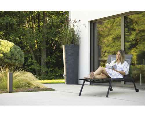 Vrouw leest boek naast regenton in de tuin.