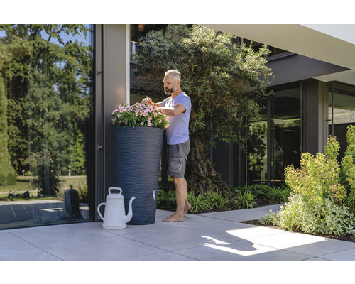 Man beplant regenton met bloemen in een tuin