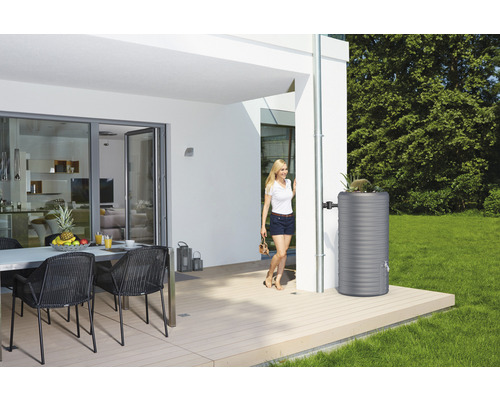 Regenwatertank van kunststof naast een regenpijp aan een modern huis met terras.