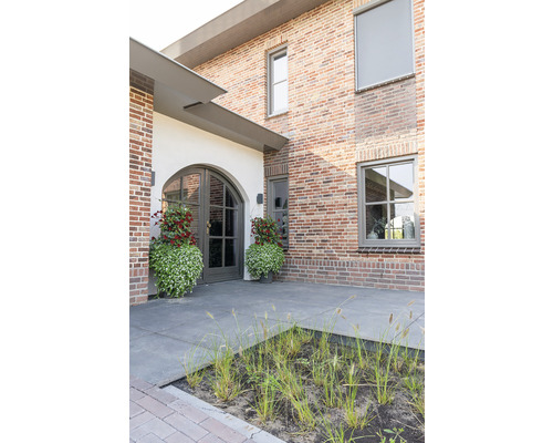 Buitenkant van een huis met bakstenen gevel, ramen, voordeur en beplanting voor het huis