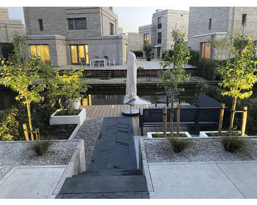 Moderne tuinontwerp met terras, tuinmeubelen en plantenbakken aan een waterweg.