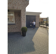 Buitenfoto van een huis met straatstenen, een plant in een pot en een jongen die met een voetbal speelt.