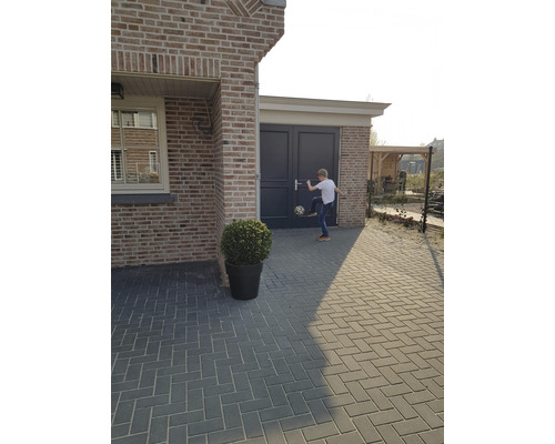 Buitenfoto van een huis met straatstenen, een plant in een pot en een jongen die met een voetbal speelt.