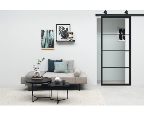 Woonkamer met glazen en stalen schuifdeur, bank, salontafels en wanddecoratie