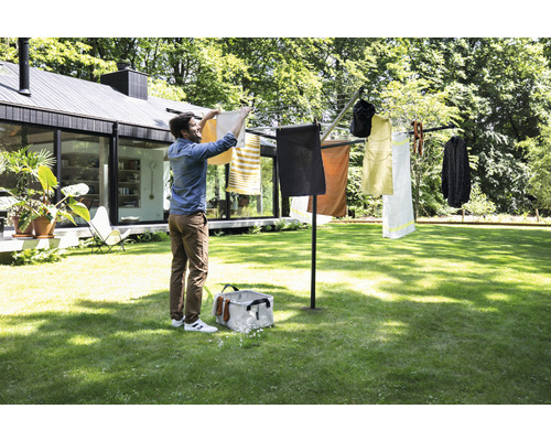 Droogmolen in de tuin met wasgoed en een persoon die het wasgoed ophangt