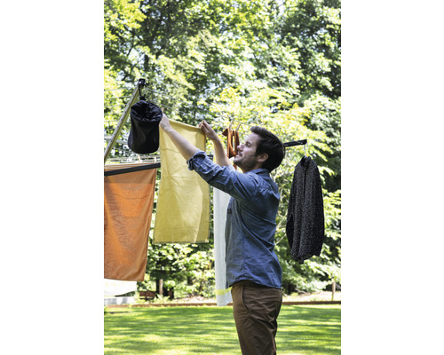 Een man hangt wasgoed te drogen op een droogmolen in de tuin.