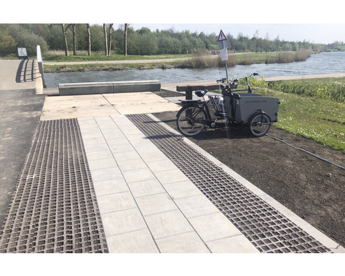 Scene met wegverharding van straatstenen en grasbetontegels naast een rivier en een driewieler