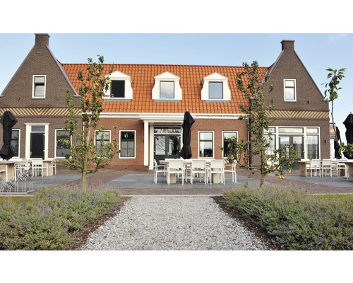 Buitenaanzicht van een gebouw met terras, tuinmeubilair en beplanting.