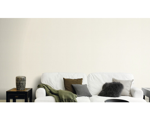 Woonkamer met witte bank, kussens en bijzettafel tegen een muur