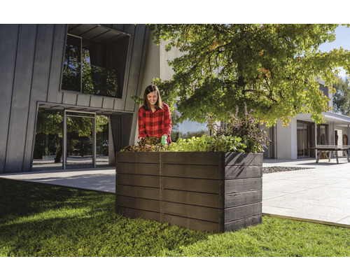 Vrouw plant een verhoogde tuinbak in de tuin voor een modern huis.