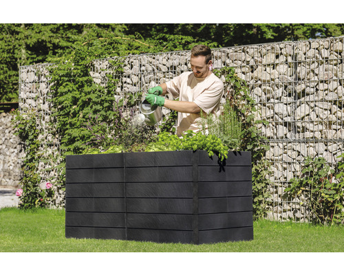 Man geeft planten water in een zwarte, verhoogde tuinbak in de tuin.