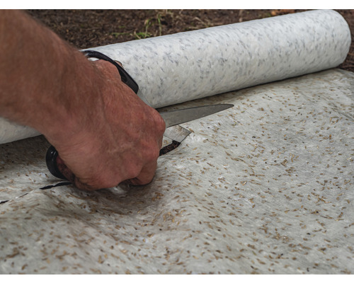 Een onkruiddoek wordt met een schaar op maat gesneden