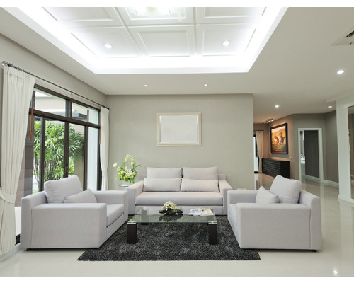 Lichte woonkamer met bank, fauteuils, glazen tafel en vloerkleed op een glanzende vloer
