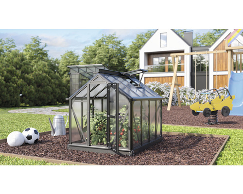 Tuinscene met kas, speeltuin en woonhuis op de achtergrond.